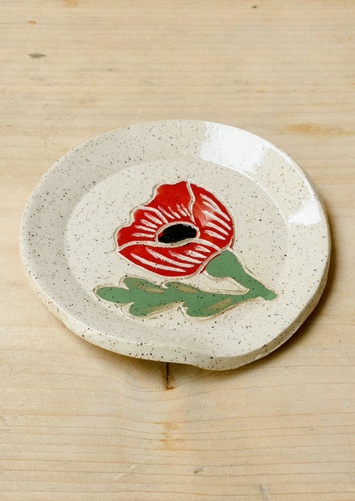 A speckled ceramic spoon rest with a single red poppy painted on it.