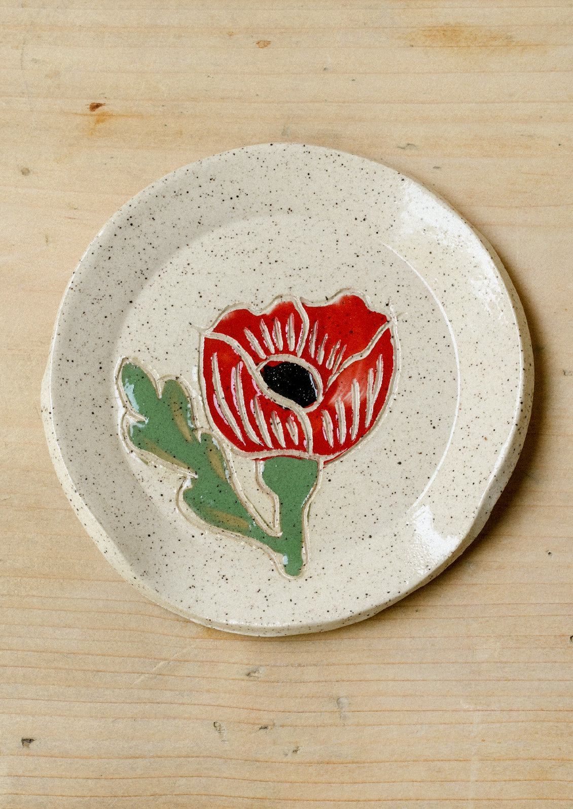 A speckled ceramic spoon rest with a single red poppy painted on it.