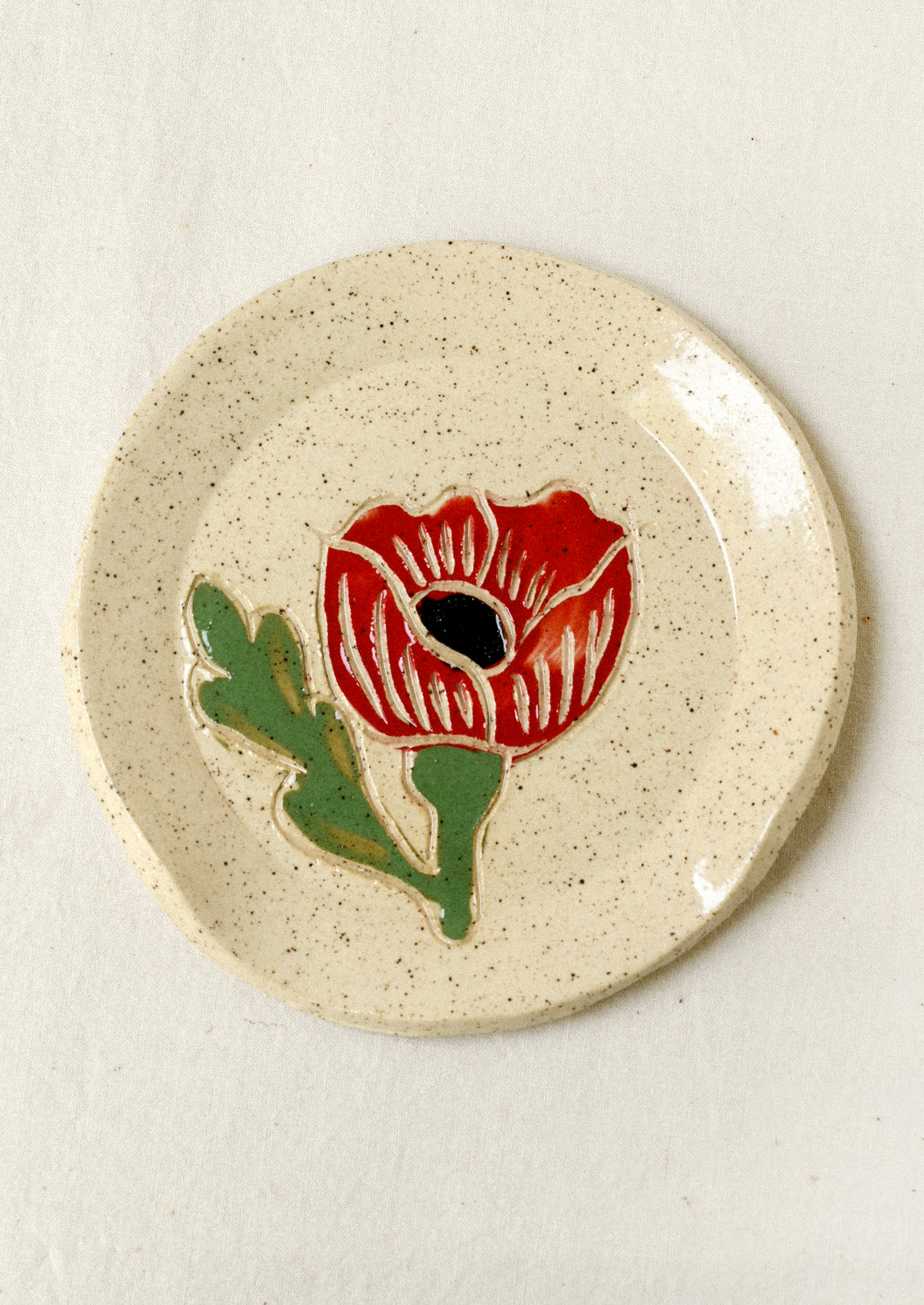 A speckled ceramic spoon rest with a single red poppy painted on it.