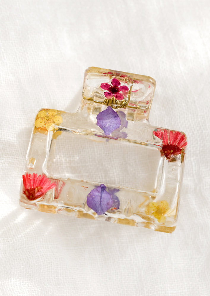 A square hair claw in clear resin with magenta dried flowers.