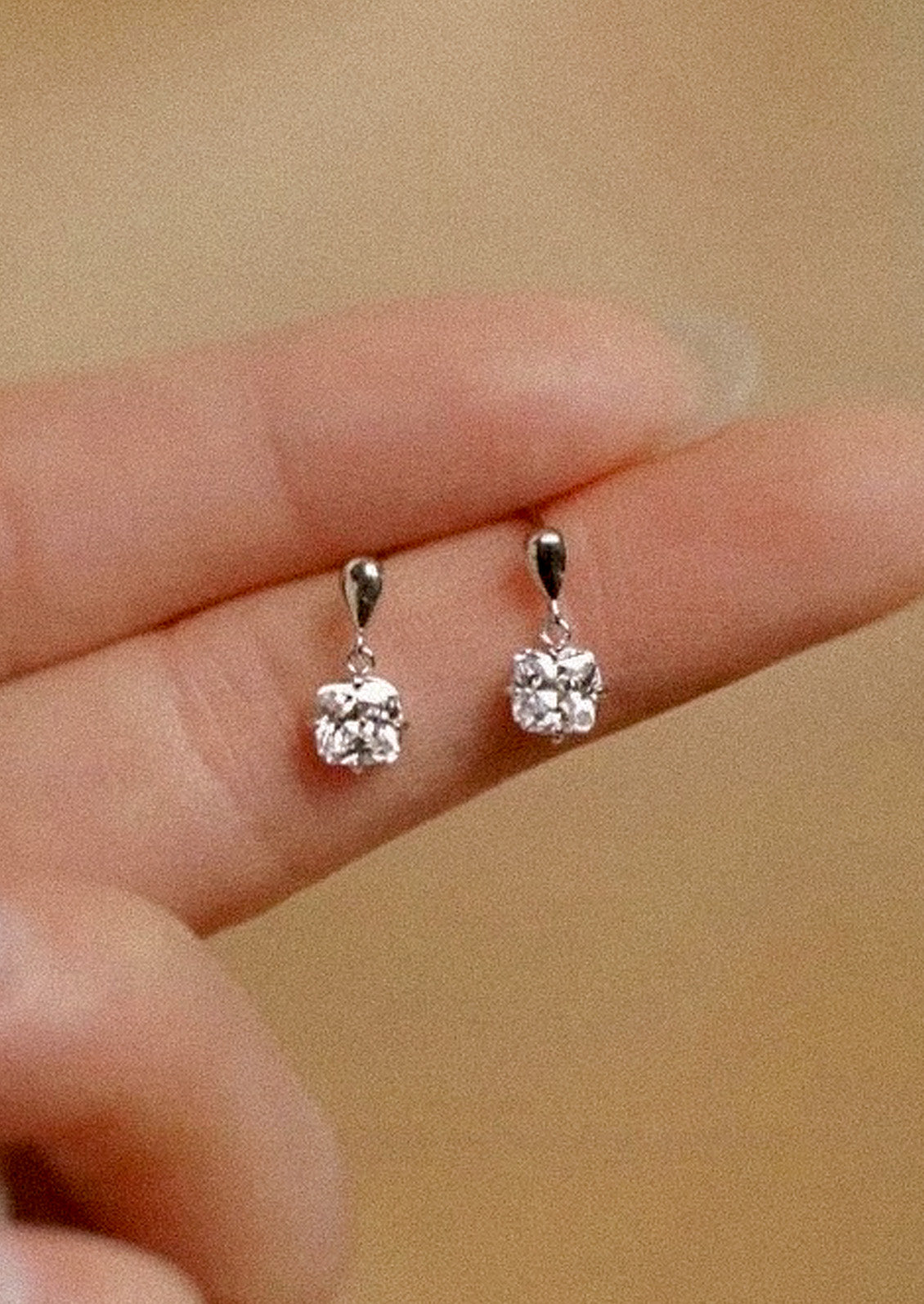 A woman holding pair of sterling silver earrings with a princess cut cubic zirconia.