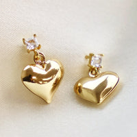 2: A pair of gold heart earrings hanging from square crystal post.