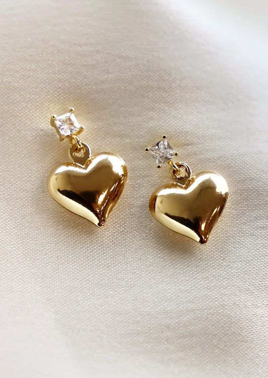 A pair of gold heart earrings hanging from square crystal post.