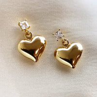 1: A pair of gold heart earrings hanging from square crystal post.