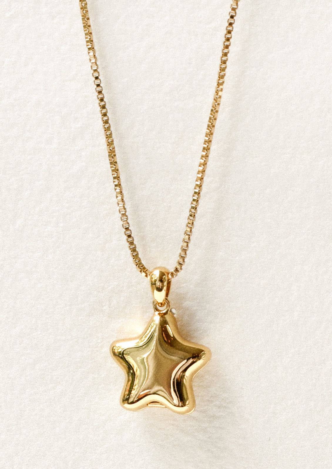 A gold necklace with a puffy star locket pendant.