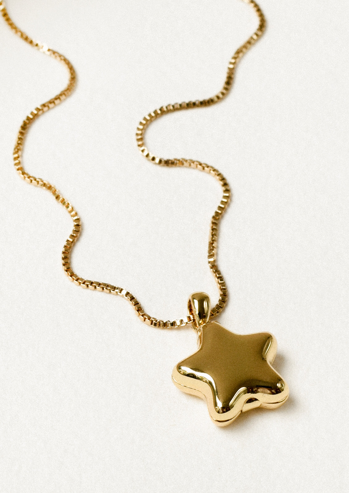 A gold necklace with a puffy star locket pendant.