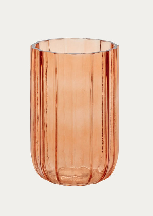 A ribbed fluted glass vase in a translucent peachy pink color.