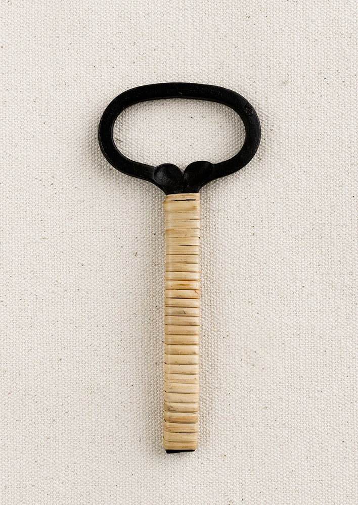 A black cast iron bottle opener with natural rattan wrapped handle.