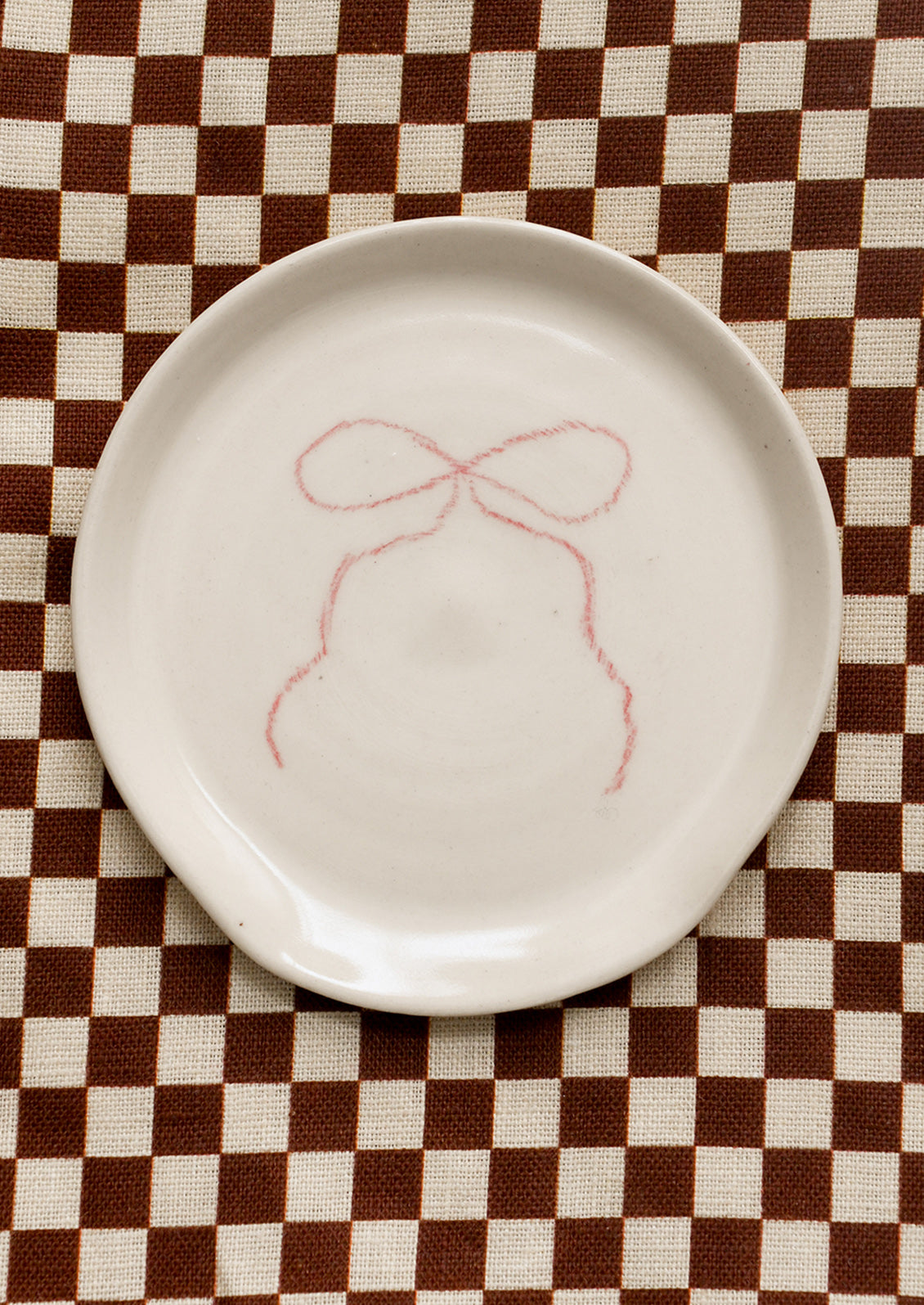 White ceramic plate with pink bow design on a brown and white checkered tablecloth