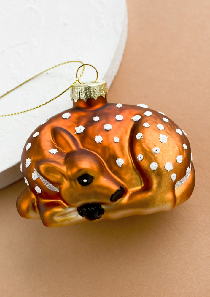 A glass holiday ornament of a curled up baby fawn.