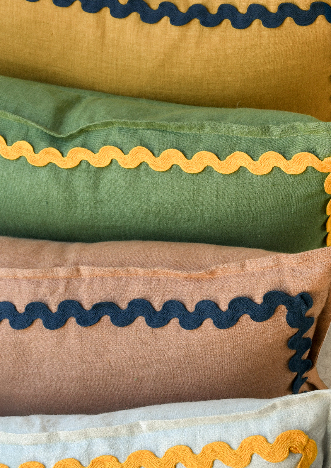 Four colorful rectangular linen pillows with a squiggle border attached along the edges.