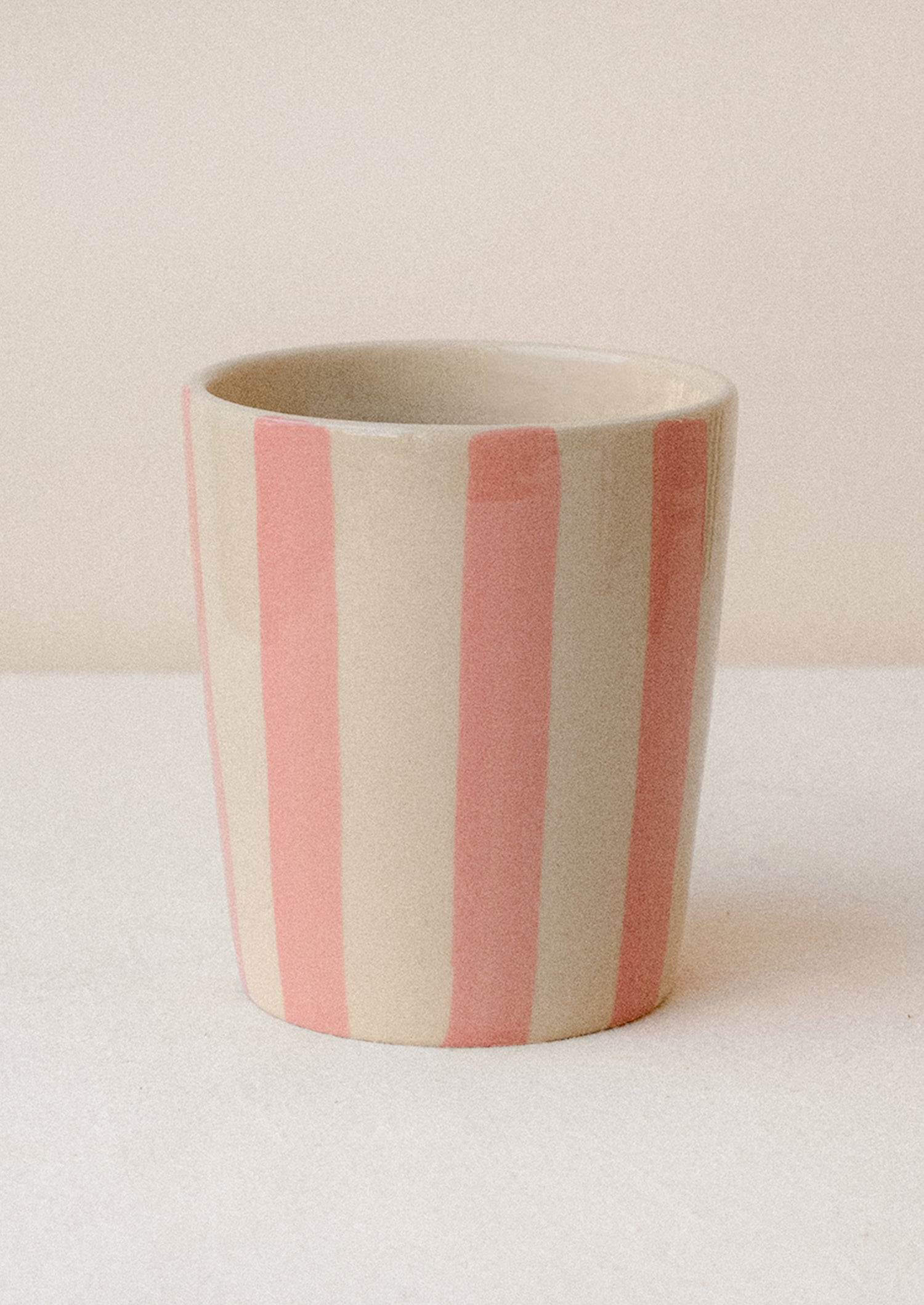A striped ceramic cup in bisque with light pink vertical stripes.