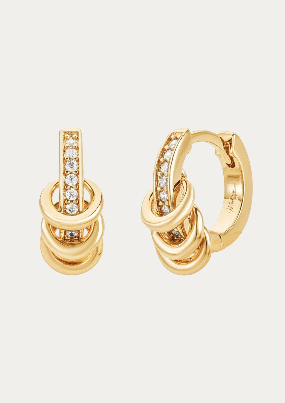 A pair of gold hoop earrings adorned with cubic zirconia gems and three ring accents on each hoop on a white background. 