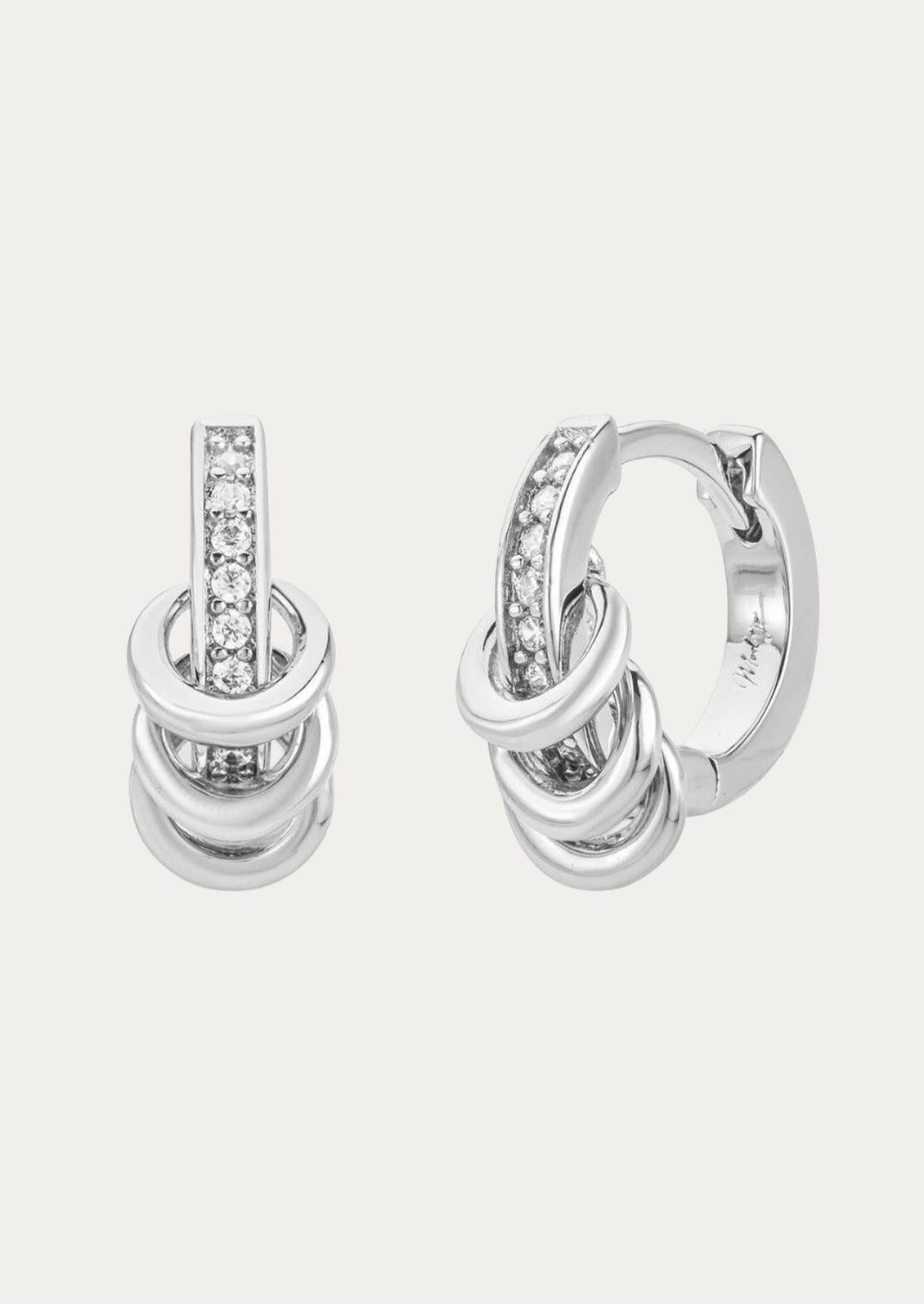 A pair of silver hoop earrings adorned with cubic zirconia gems and three ring accents on each hoop on a white background. 