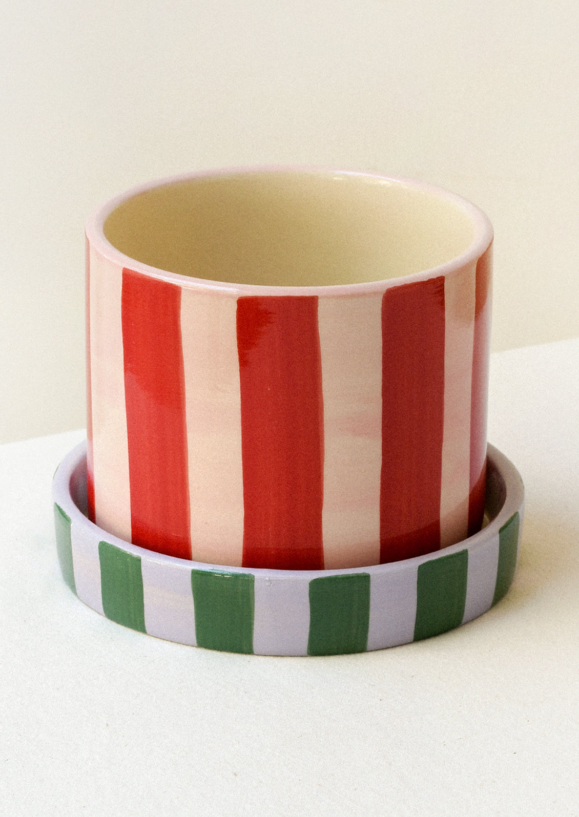 A colorful red and pink striped ceramic planter with a striped green and purple saucer.