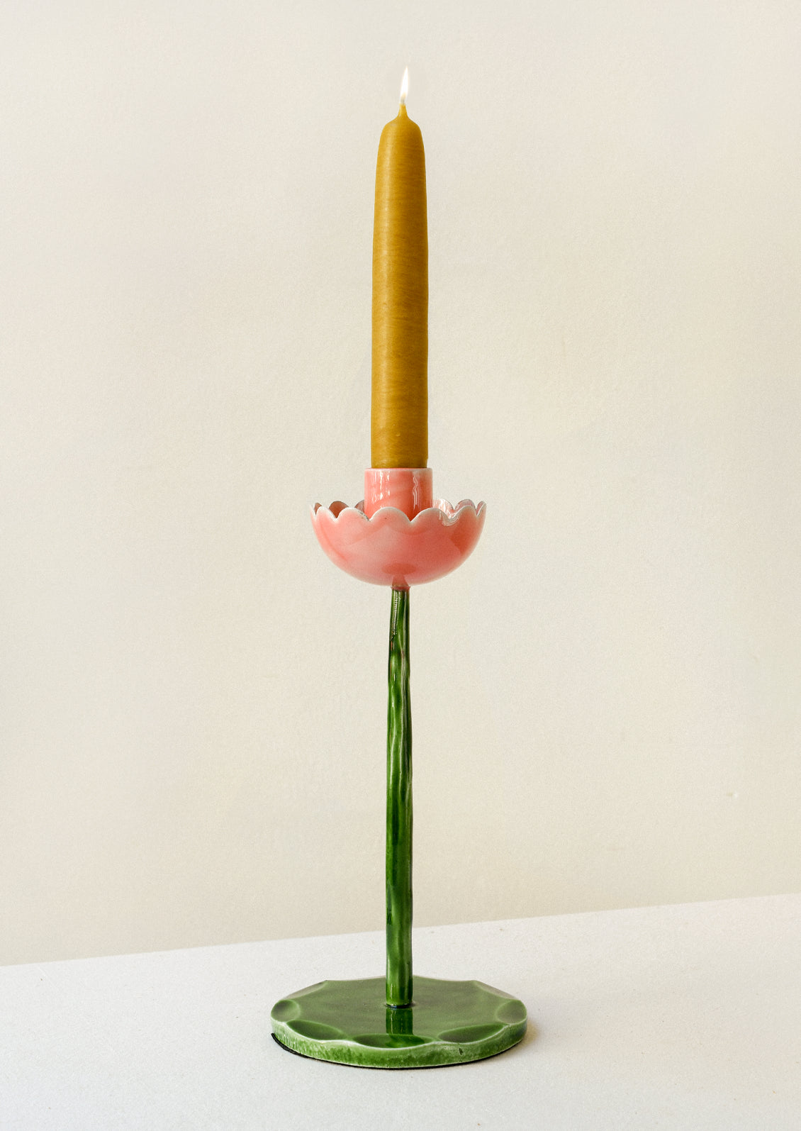 A taper holder in the shape of a flower with a pink top and green stem/base.