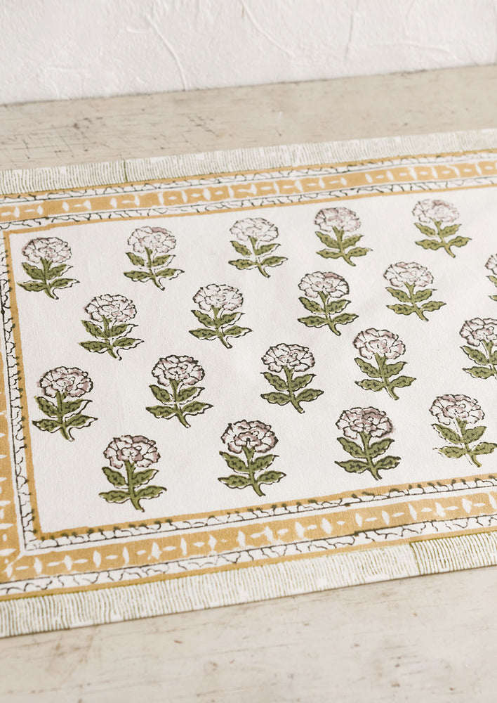 A block printed placemat in floral print in green and purple with mustard border.