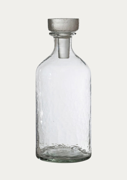 A round bottle in clear glass with pebbled texture and glass stopper.