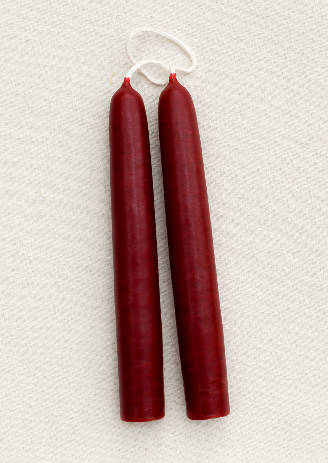 A pair of short ruby red taper candles on a brown background.