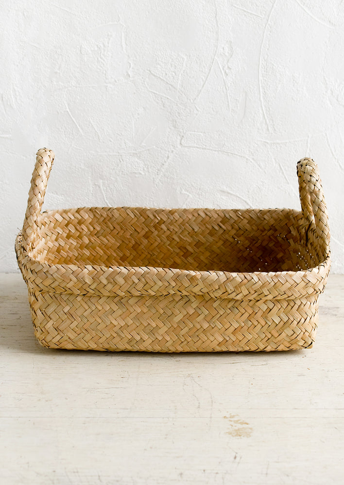 A rectangular seagrass basket with rolled top rim and side handles.