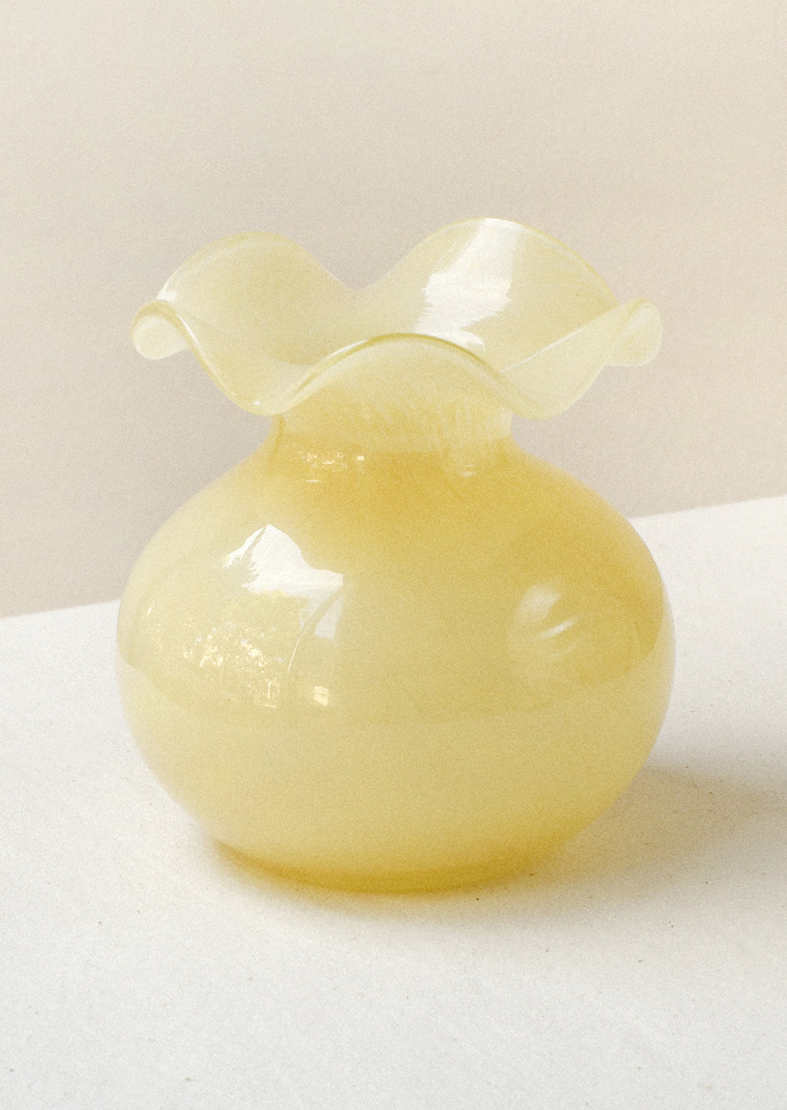 A glass bud vase in cream-yellow color with ruffled opening.