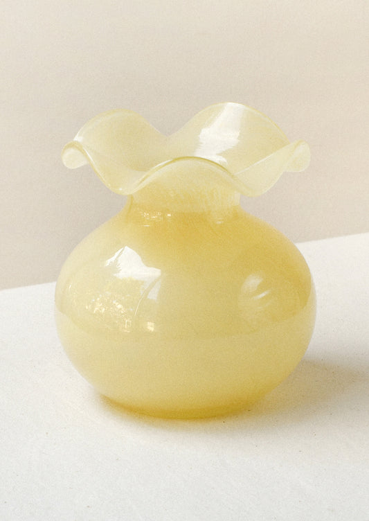 A glass bud vase in cream-yellow color with ruffled opening.