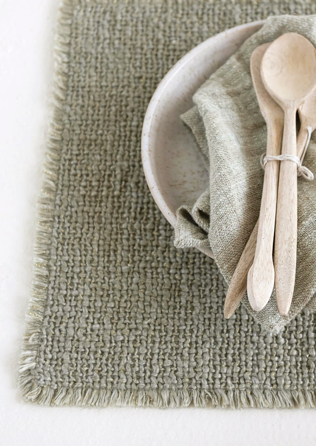 4: A sage green placemat with fringe edges.