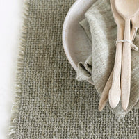 4: A sage green placemat with fringe edges.