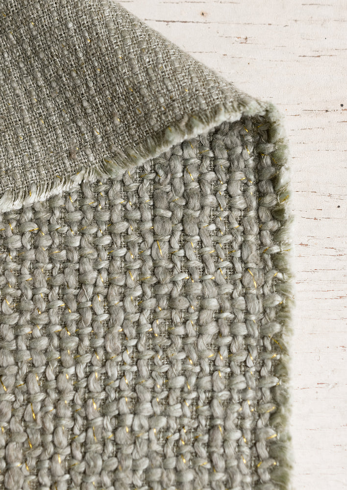 A sage green placemat with fringe edges.