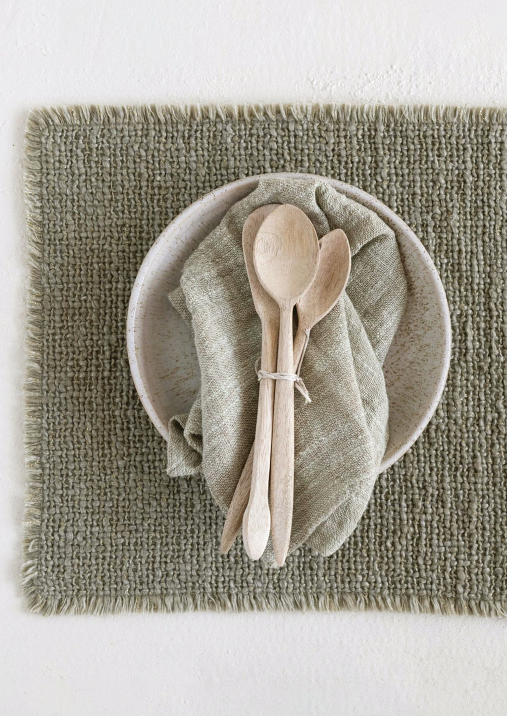 1: A sage green placemat with fringe edges.