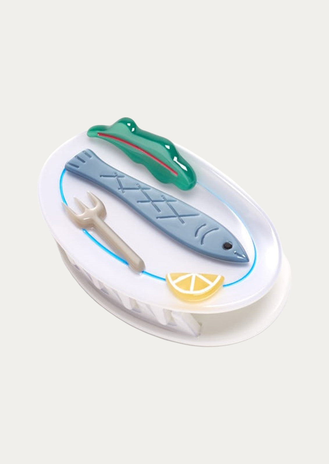 A white claw clip with a sardine, lettuce leaf, fork, and lemon slice on top on a white background.