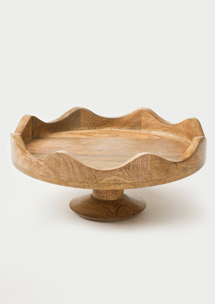 A mango wood cake stand with scalloped wavy edges.