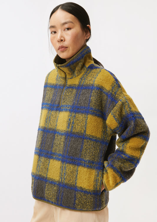 A woman wearing a fleece pullover in olive and cobalt blue plaid pattern.