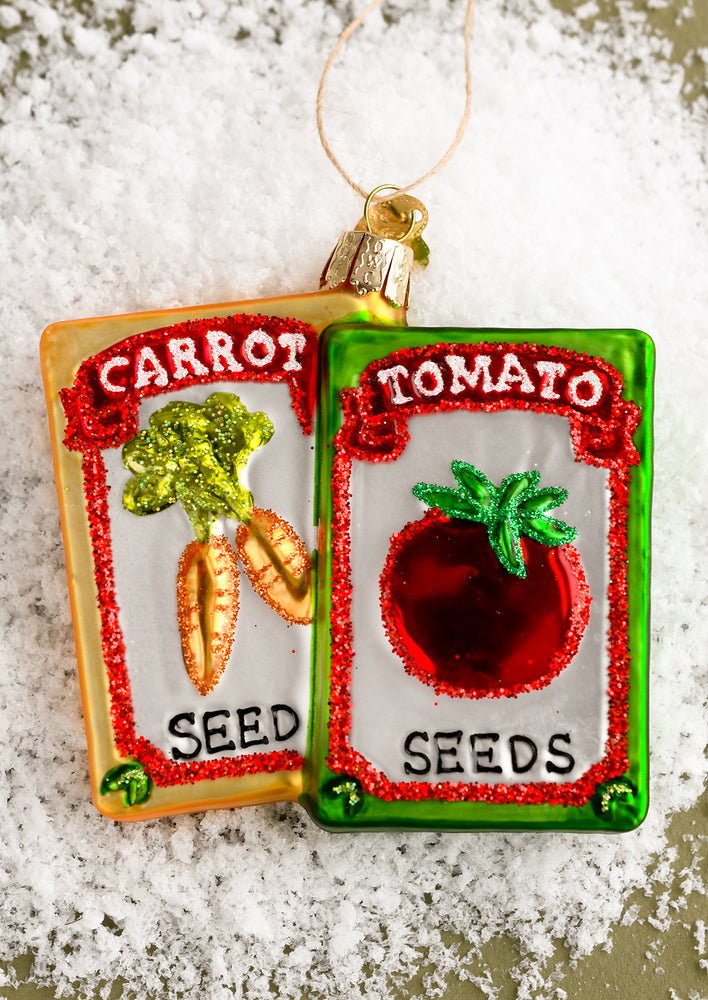 A glass holiday ornament of packets of carrot and tomato seeds.