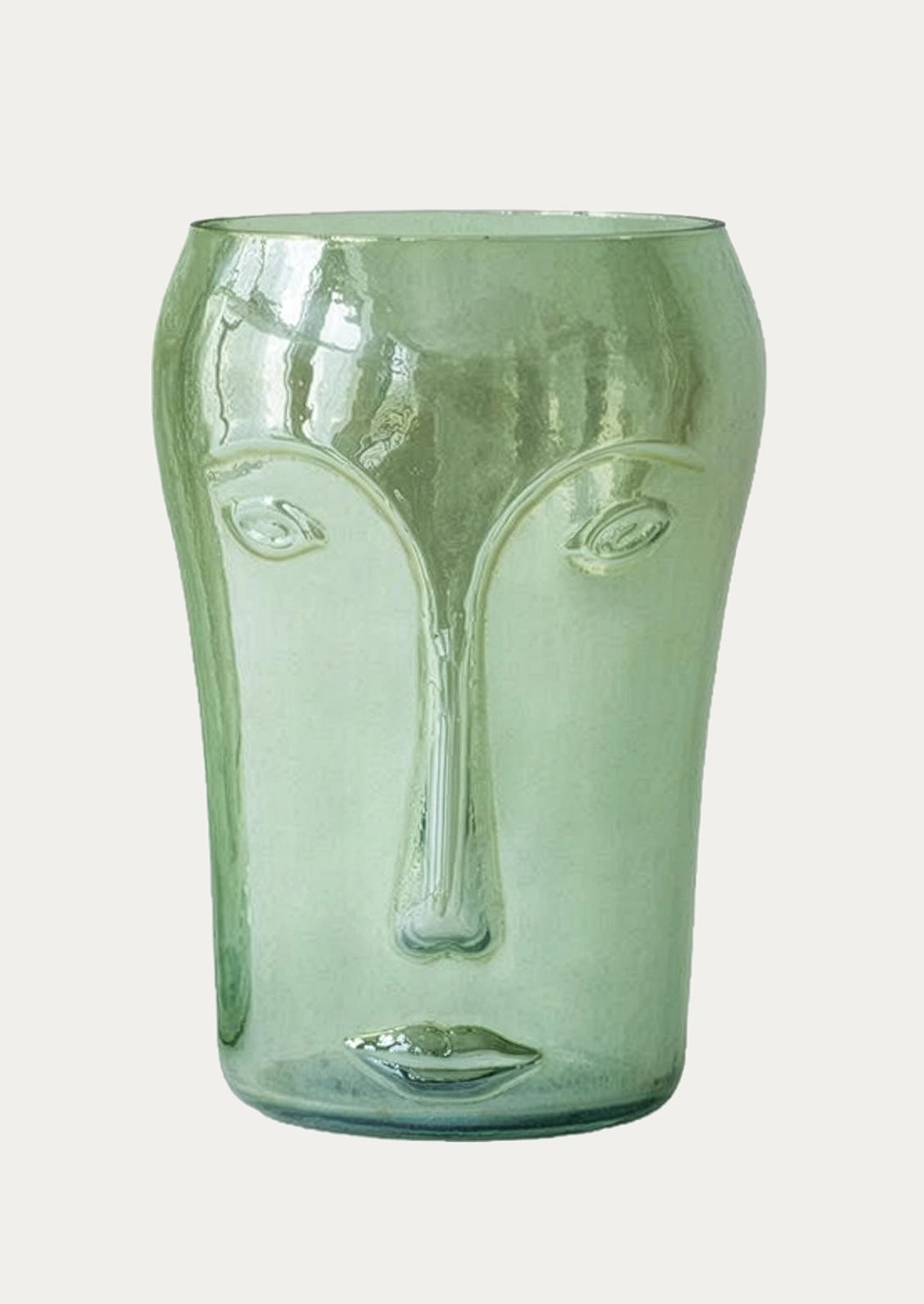 A translucent sage green glass vase shaped like a stylized face, photographed against a solid off-white background.