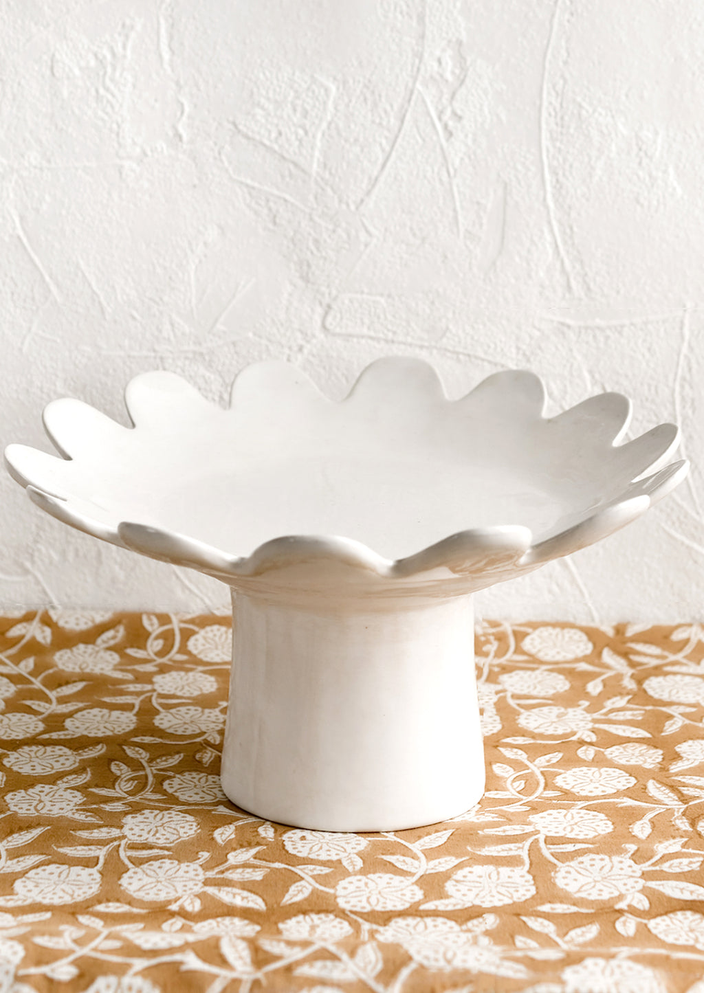1: A pedestal riser in gloss white ceramic with scalloped plate shape.