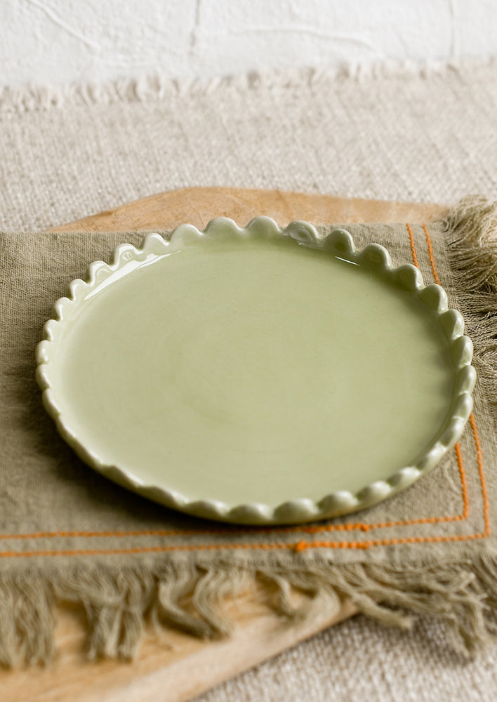 A round ceramic plate in green with scalloped edges.