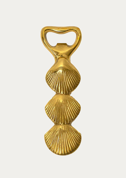 Gold bottle opener with shell design on a white background
