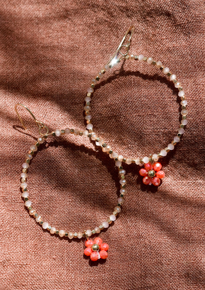 A pair of beaded hoop earrings with flower charm in peach.