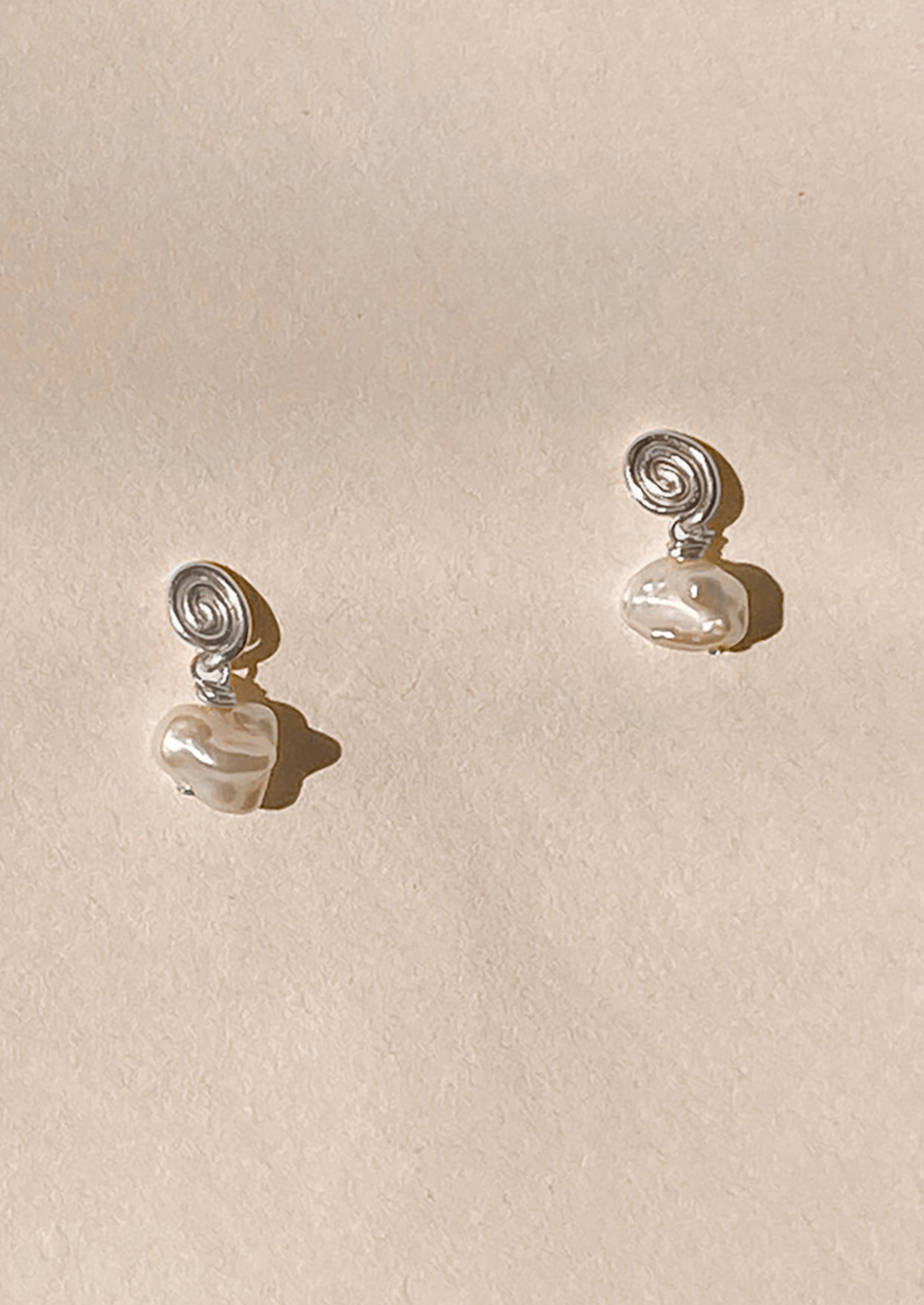 Pair of silver earrings with pearl-like beads on a beige background
