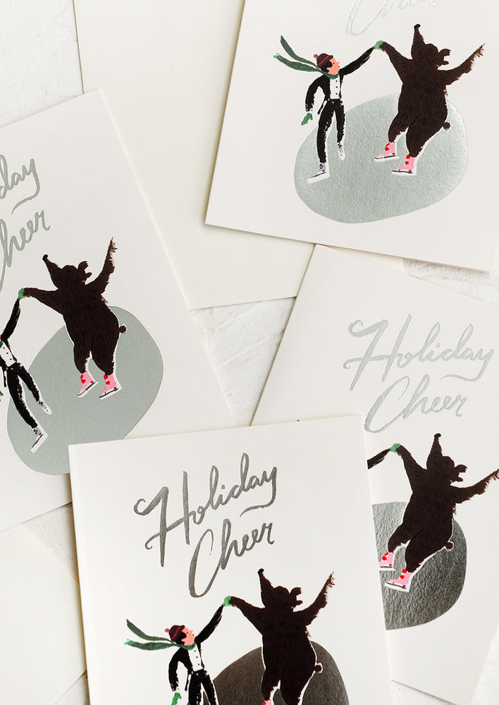 A set of cards depicting an ice skater and bear skating on silver pond, text reads "Holiday cheer".