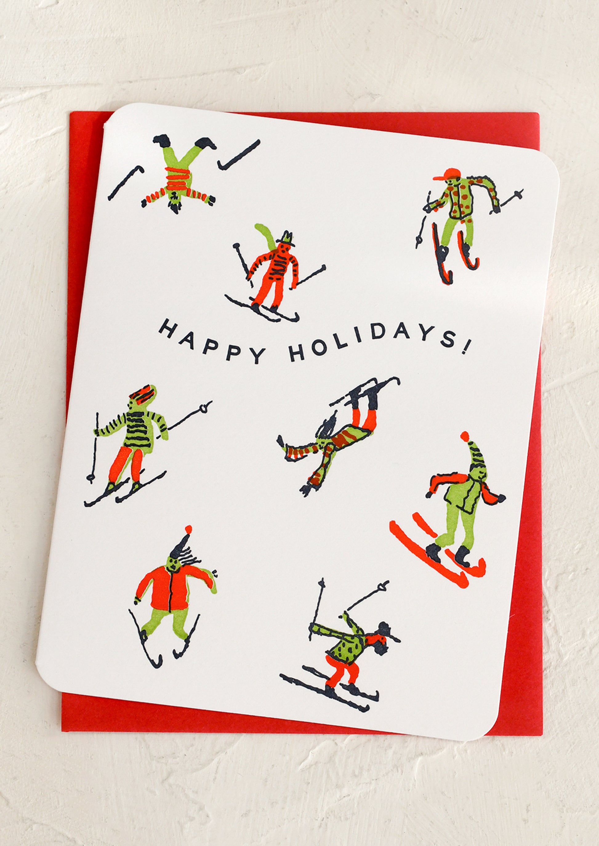 Greeting card with skier illustrations and 'Happy Holidays!' text on a red envelope.