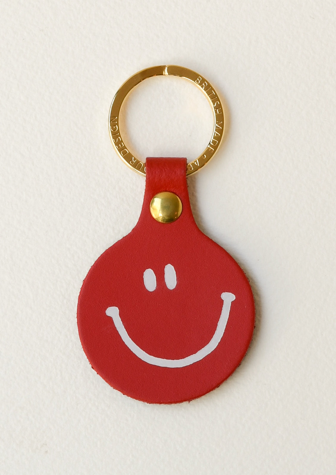 A red leather circle keychain with a smiley face on the front on a gold key ring.