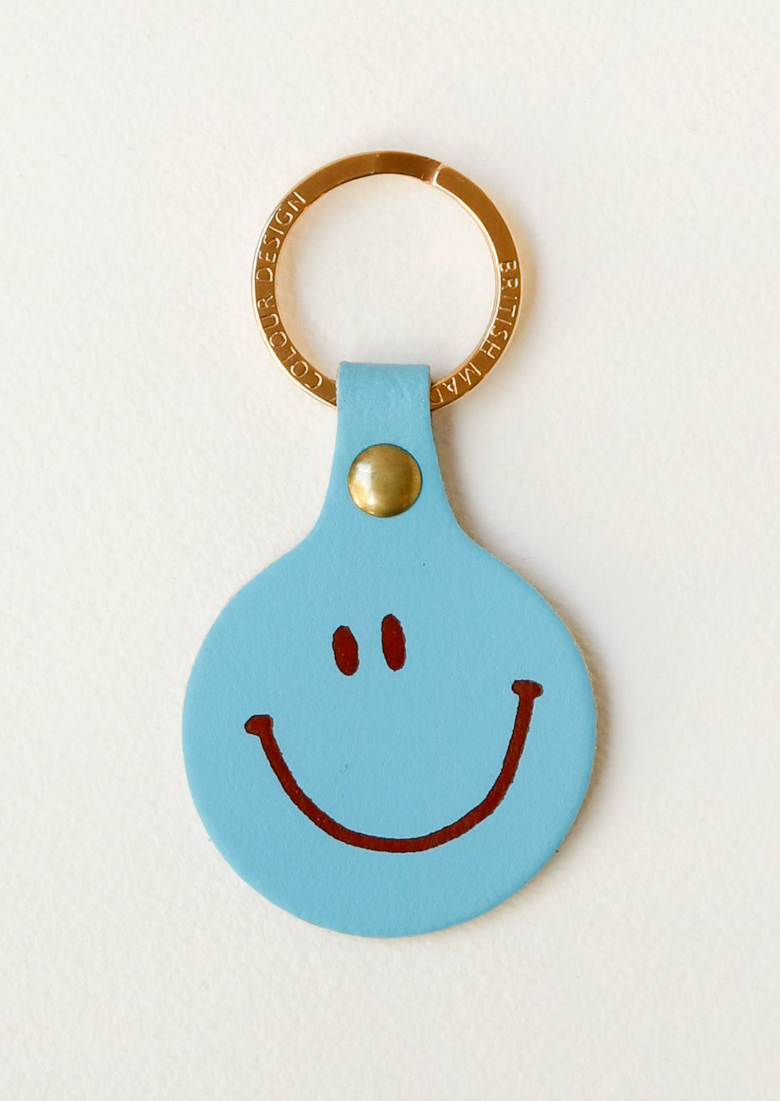 A turquoise leather circle keychain with a smiley face on the front on a gold key ring.