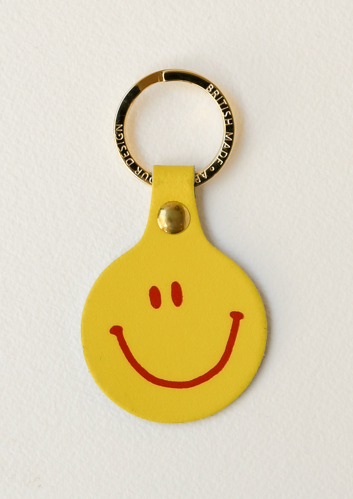 A yellow leather circle keychain with a smiley face on the front on a gold key ring.