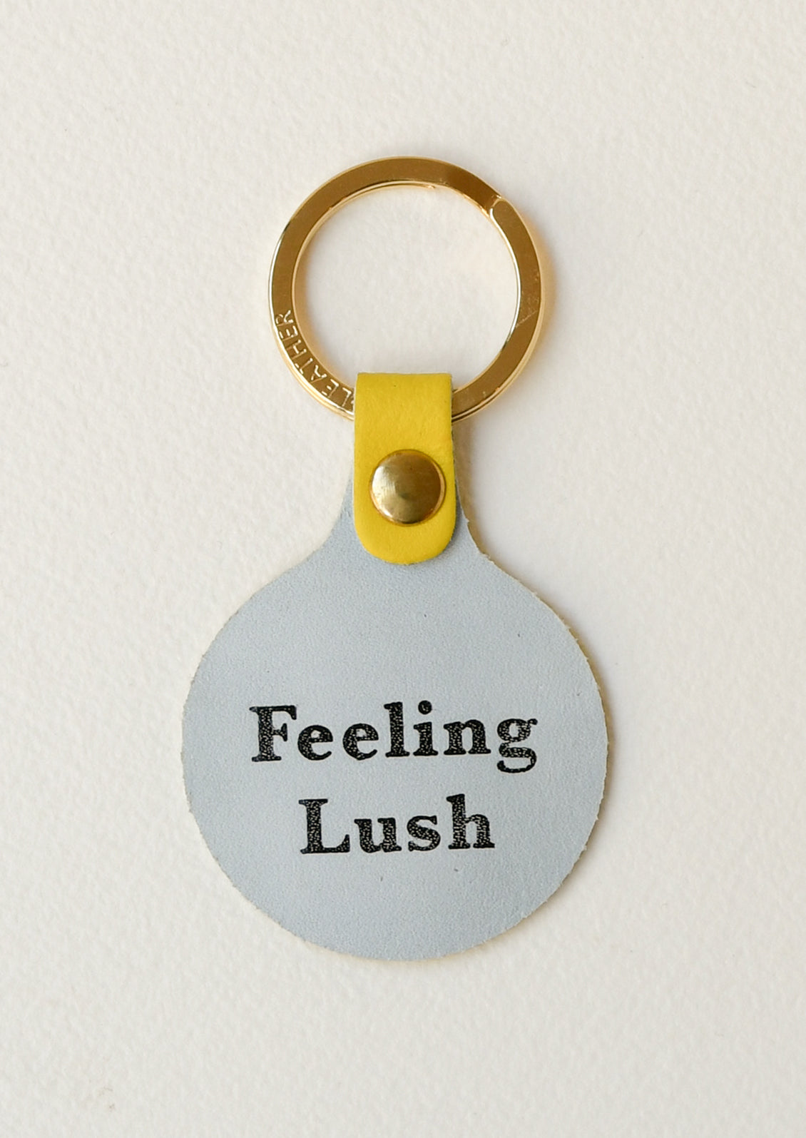 The back of a yellow leather circle keychain with the words "Feeling Lush" on the back on a gold key ring.