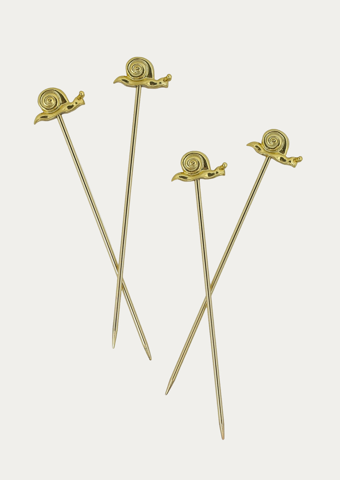 Four gold-toned cocktail picks with sculpted snail tops, arranged on a light gray background.