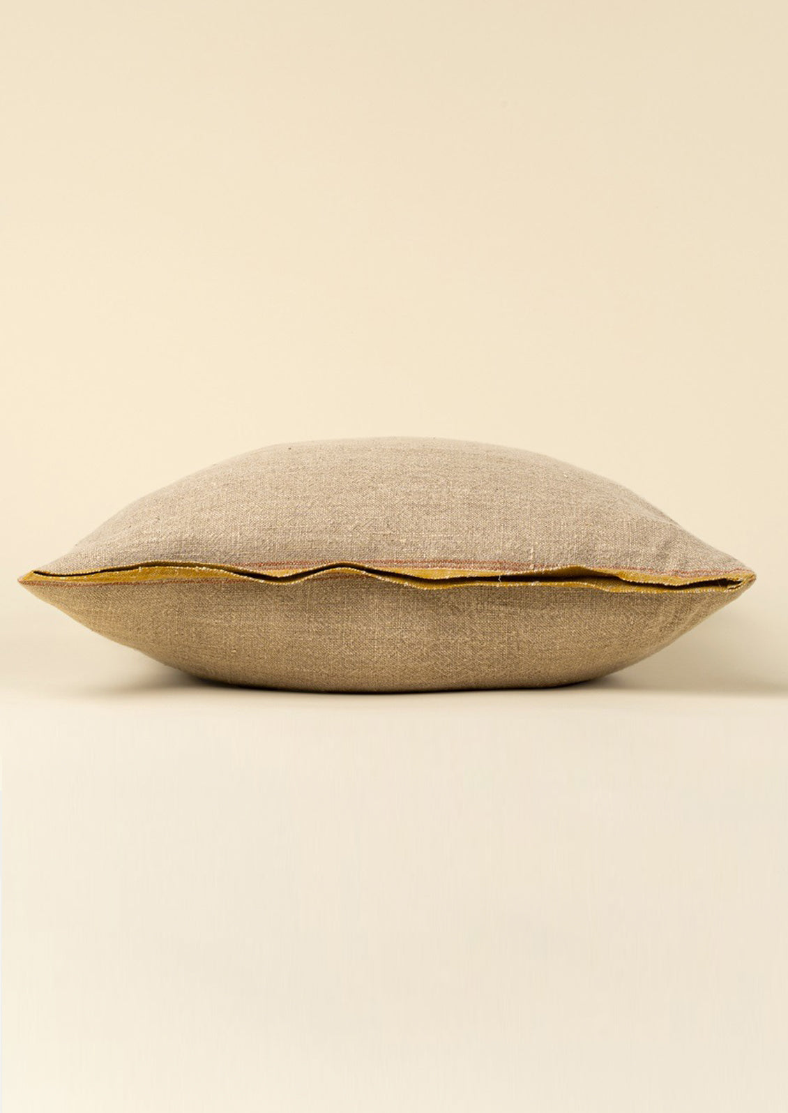 A natural linen throw pillow with mustard decorative selvage trim.