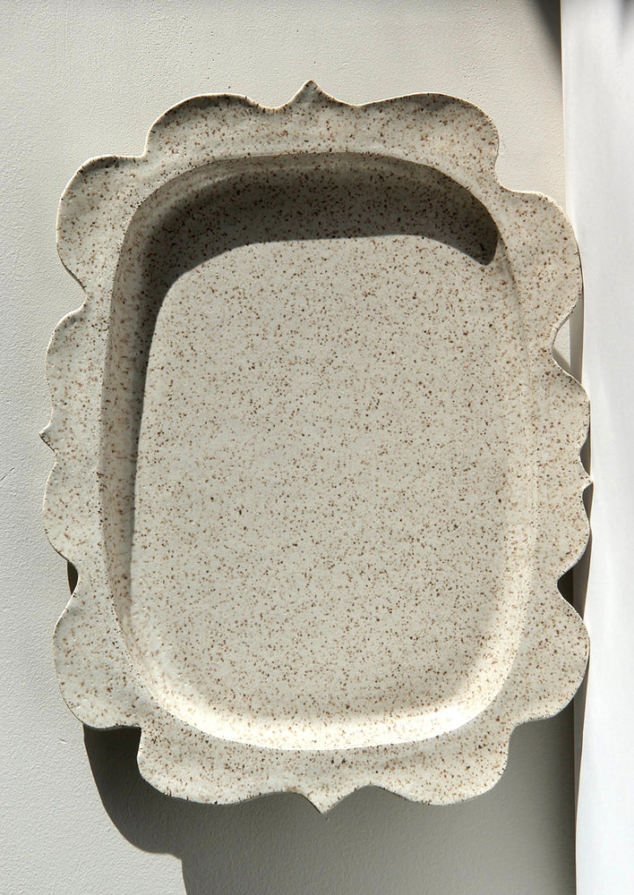 A rectangular shaped platter in speckled cream ceramic with wavy shape edge.