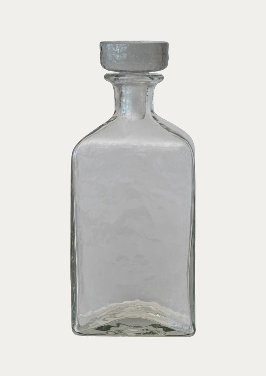 A square bottle in clear glass with pebbled texture and glass stopper.